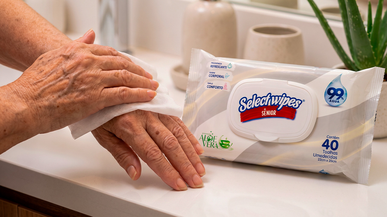 Mão de cuidador segurando uma embalagem de toalha umedecida para idosos da Linha Sênior HIGIECARE, ideal para pele madura e sensível.